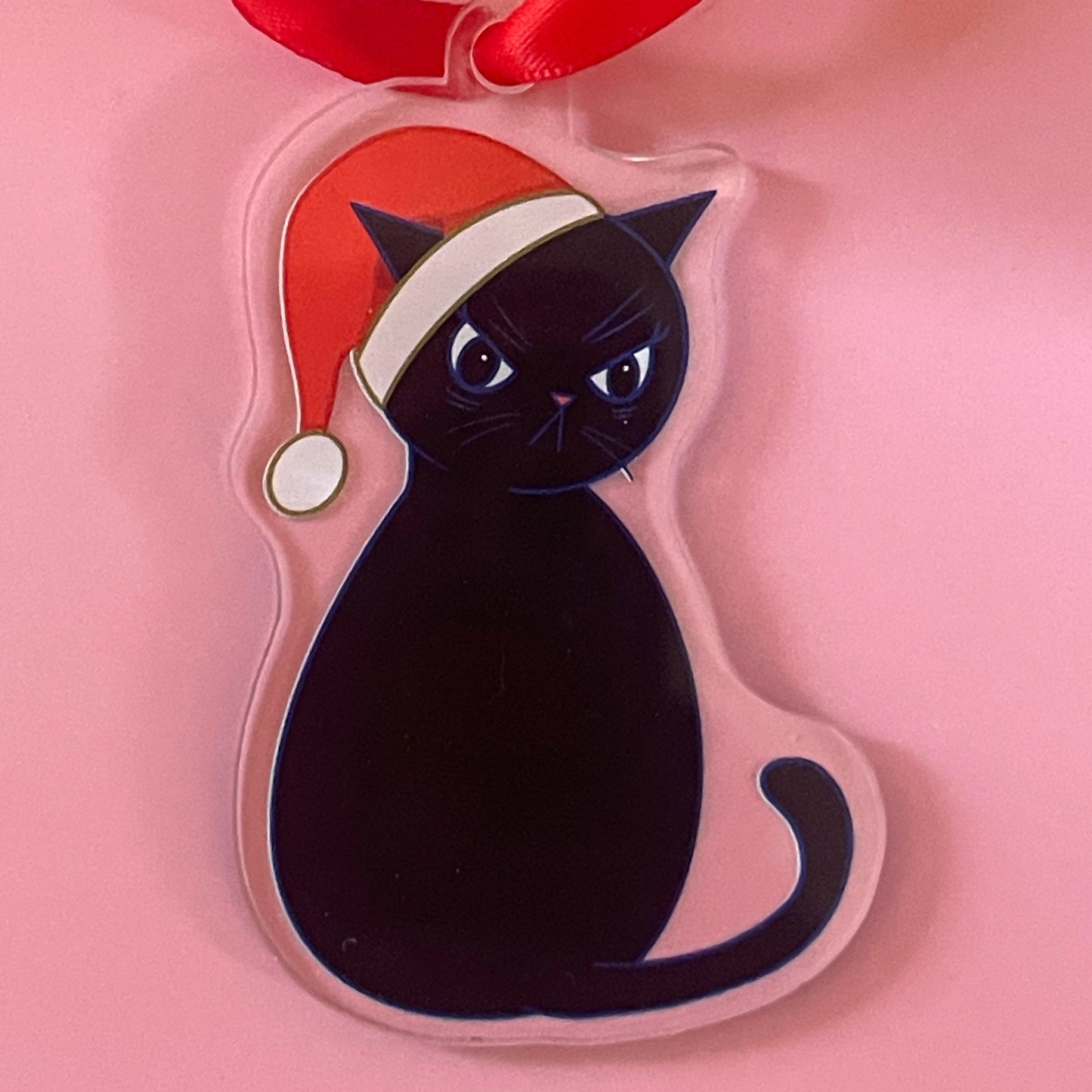 Grumpy black cat with a Santa hat on a pink background