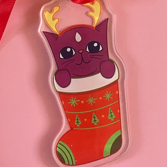 Purple cat with reindeer antlers in a red Christmas stocking on a pink background