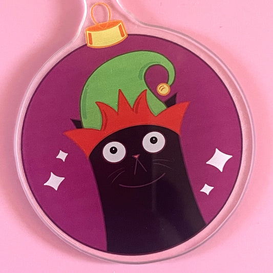 Circular ornament with a black cat wearing an elf hat on a pink background